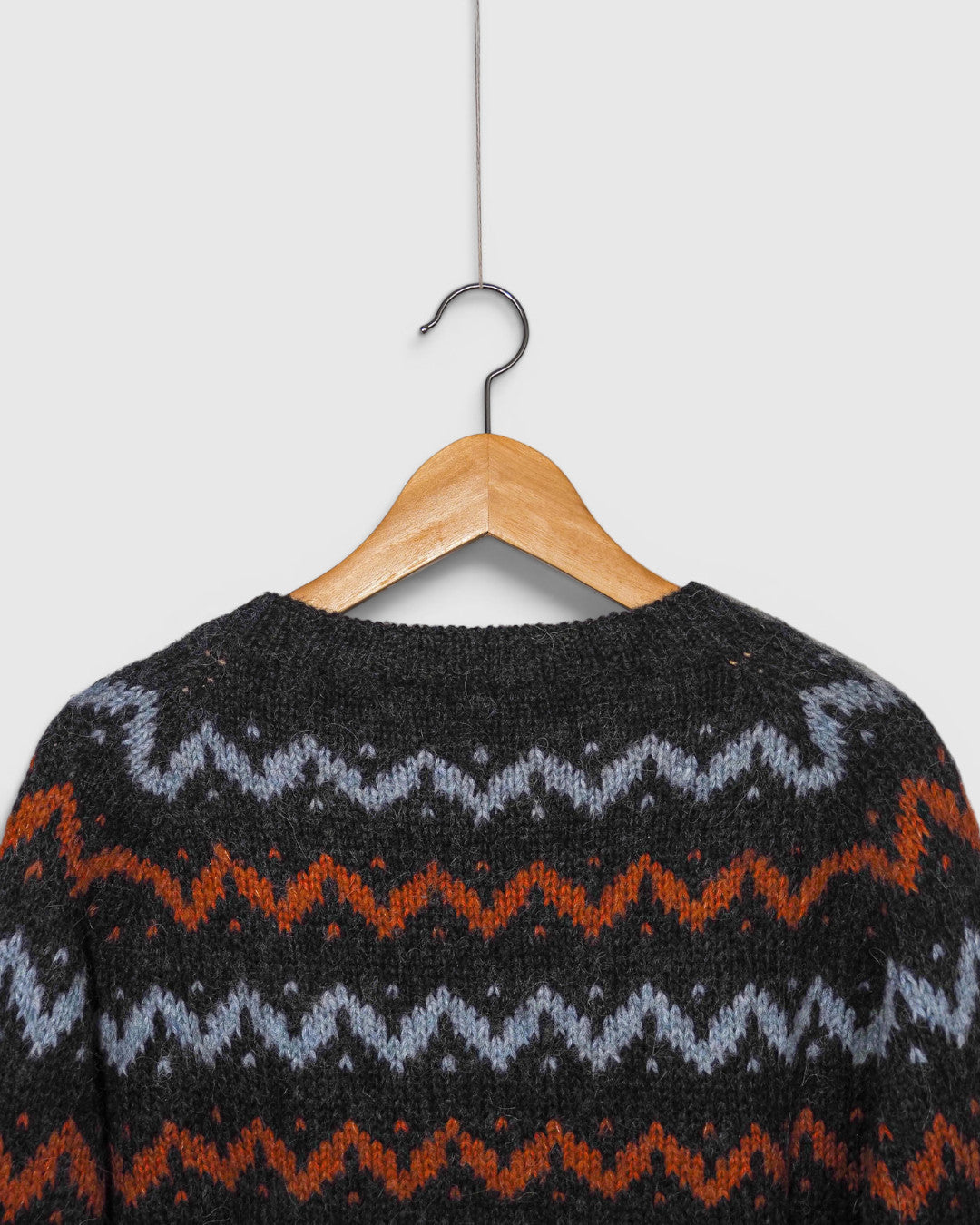Cárdigan de punto Lalura Design con patrón geométrico en zigzag gris, azul y naranja colgado en percha de madera